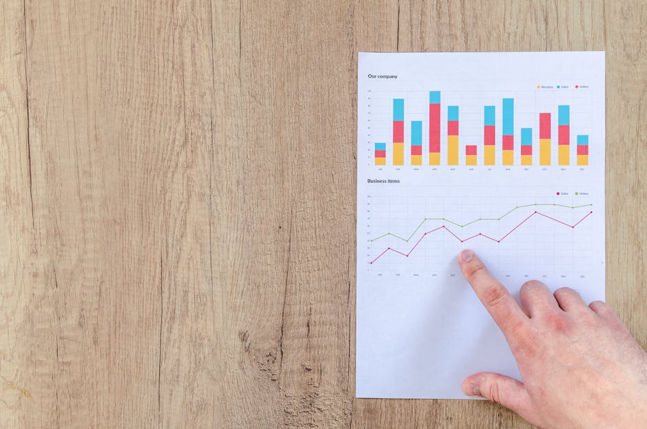 Hand analyzing business graphs on a wooden desk, focusing on data results and growth analysis