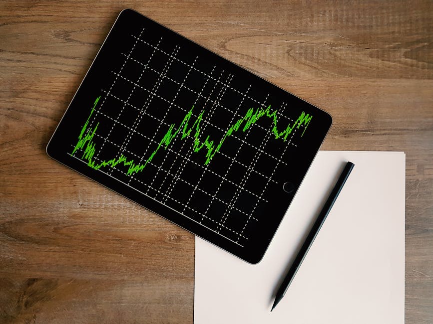 Flatlay of an iPad displaying stock market graph on a wooden desk with a pencil and paper